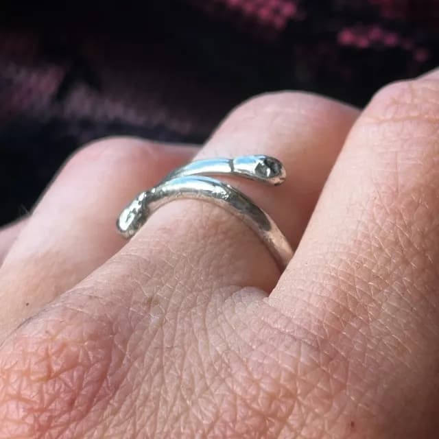 Vue latérale rapprochée d'une bague spirale argentée façon allumette portée au doigt.