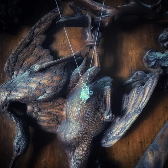 Collier en chaîne fine et pendentif opale en argent, suspendu sur un oiseau en bois sculpté.