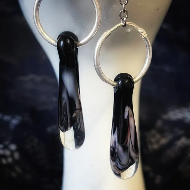Gros plan sur les pendentifs gouttes en verre filé noir et translucide montés sur créoles