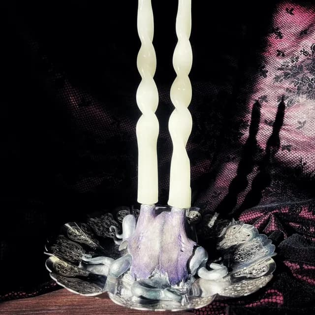 Bougeoir avec deux bougies torsadées montées sur un crâne teinté violet et une coupelle en métal ouvragé.