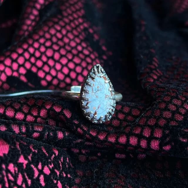 Bague avec pierre blanche en goutte sertie de griffes ciselées sur tissu résille noir et fuchsia.