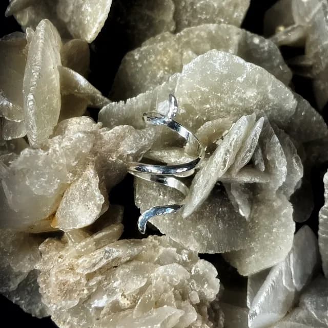 Bague spirale argentée posée sur une roche minérale cristallisée aux teintes beiges.