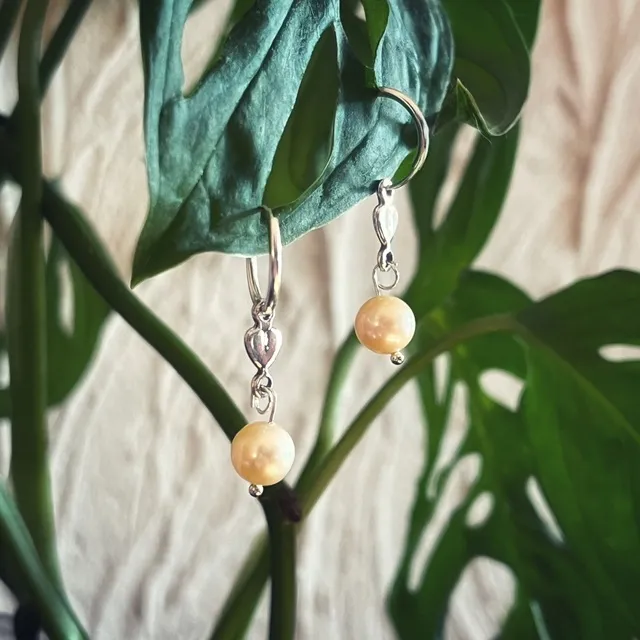 Créoles en argent ornées d'un cœur et d'une perle d'eau douce suspendues à une feuille verte.