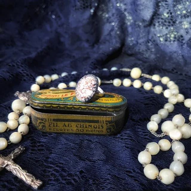 Bague argentée avec pierre sertie sur une boîte ancienne entourée d'un chapelet.
