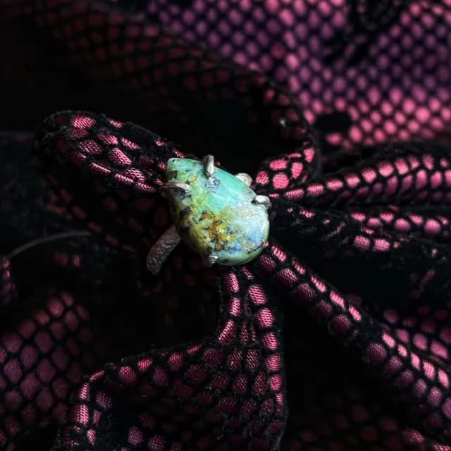 Bague réglable en argent avec jaspe africaine bleu-vert en goutte, posée sur un tissu noir et rose.