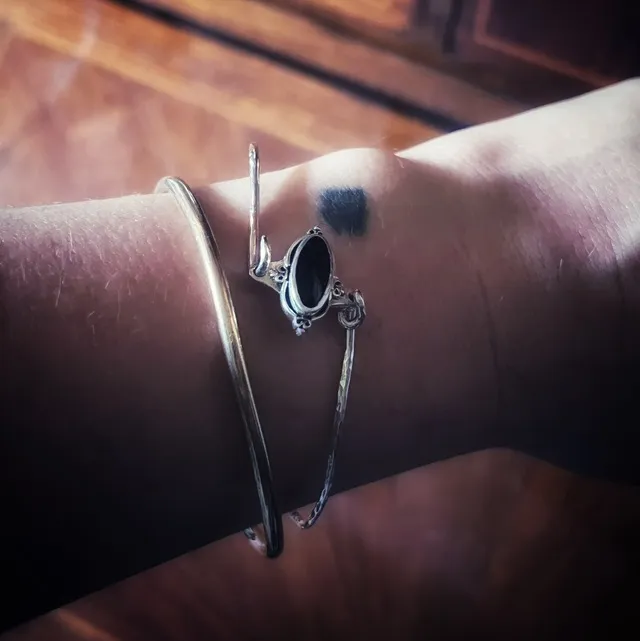 Bracelet jonc argenté et pierre noire ovale porté au poignet