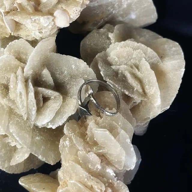 Vue plongeante de la bague ajustable flèche et cœur posée sur une roche beige.