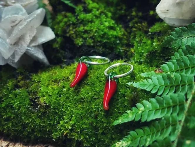 Boucles d'oreilles créoles ornées de petits piments rouges posées sur un lit de mousse
