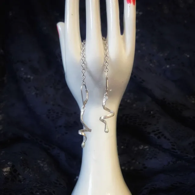Paire de boucles d'oreilles en spirale argentée présentées sur une main en céramique blanche