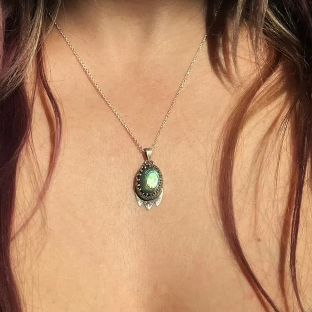 Pendentif en argent serti d'un cabochon d'abalone aux reflets verts et bleus, porté en collier.