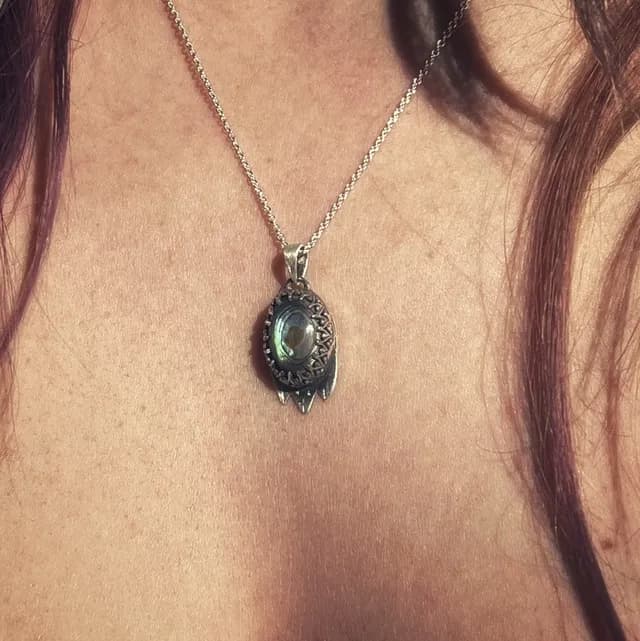 Gros plan sur le pendentif serti d'une nacre abalone ovale aux nuances irisées et sa bélière ouvragée.