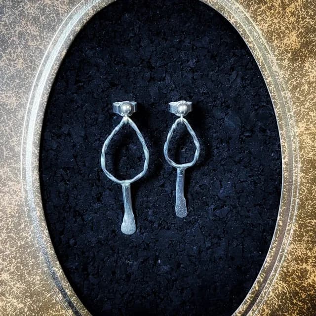 Boucles d'oreilles argentées aux formes organiques asymétriques fixées sur fond noir.