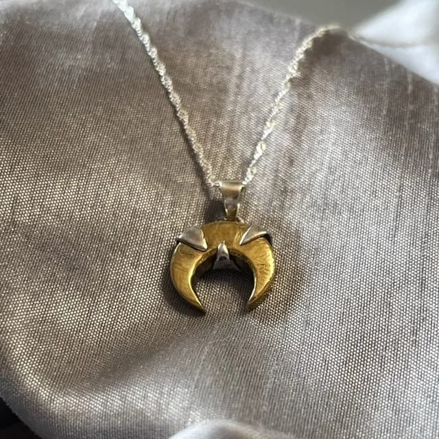 Pendentif lune inversée dorée serti d'argent et sa chaîne argentée posés sur un tissu soyeux.