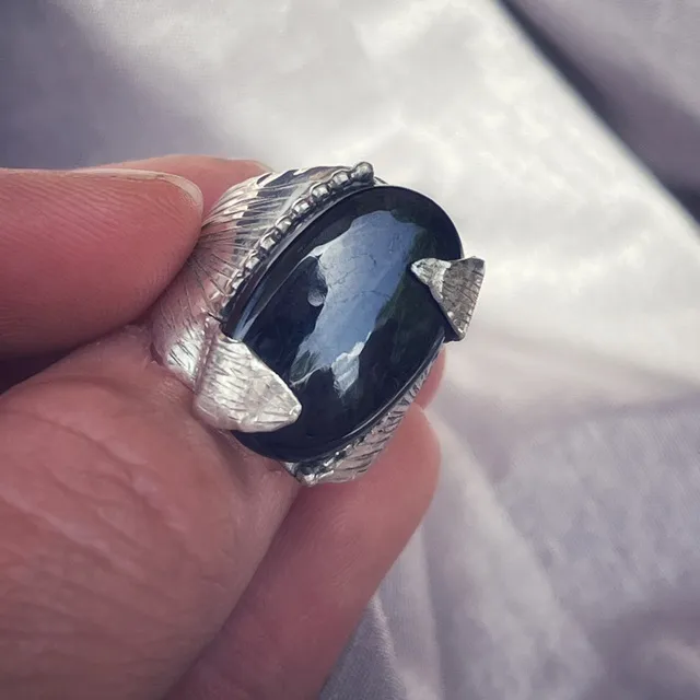 Bague volumineuse en argent à motif gravé avec cabochon sombre tenue en main