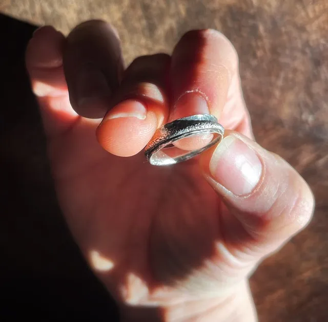 Bague argentée martelée avec anneau mobile tenue entre les doigts à la lumière naturelle.