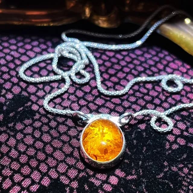 Gros plan sur le cabochon d'ambre translucide serti d'argent et sa chaîne argentée travaillée.