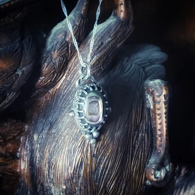 Pendentif relique en argent et nacre d'abalone suspendu à sa chaîne fine sur une sculpture en bois.