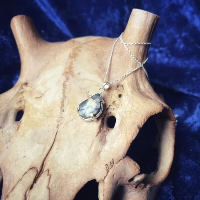 Pendentif goutte en argent et pierre naturelle sur fine chaîne argentée posé sur un support en os texturé.