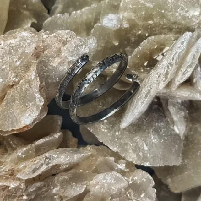 Bague de phalange spirale en argent avec motifs végétaux, posée sur une roche minérale.