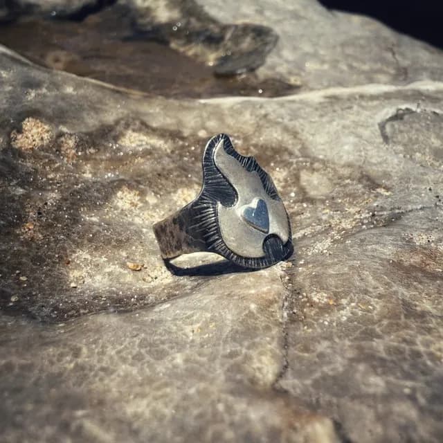 Vue de côté de la bague argentée ajustable motif flamme et cœur sur fond minéral.