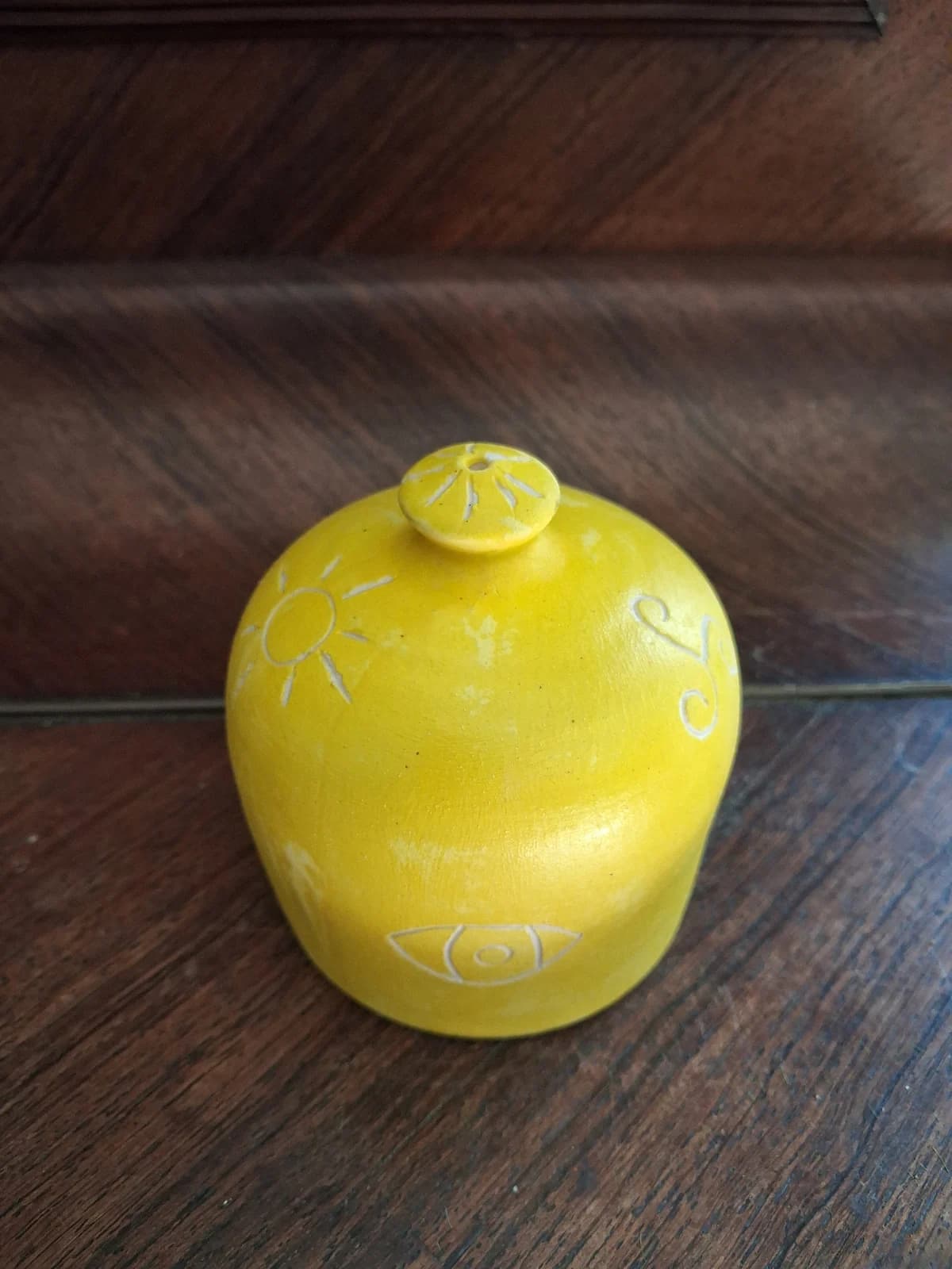 Pièce arrondie en céramique jaune avec petite prise et gravures blanches de soleil et d'œil.