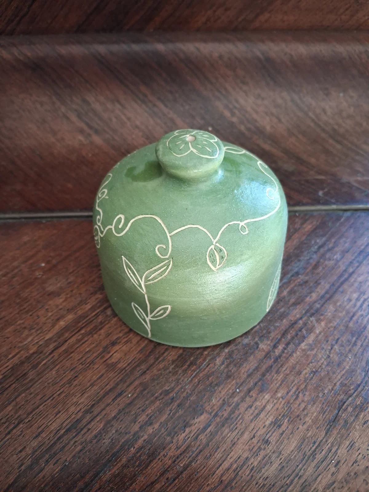 Arrosoir-main en céramique vert tendre aux motifs végétaux et volutes blanches gravées.