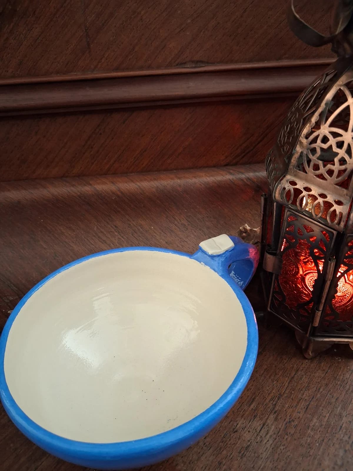 Vue plongeante d'une tasse en céramique évasée bleue à intérieur clair et anse ornée d'un petit livre