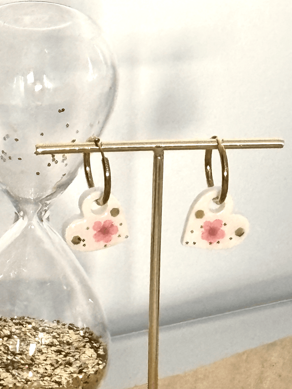 Gros plan sur les créoles dorées aux cœurs fleuris suspendues à un présentoir en métal doré.