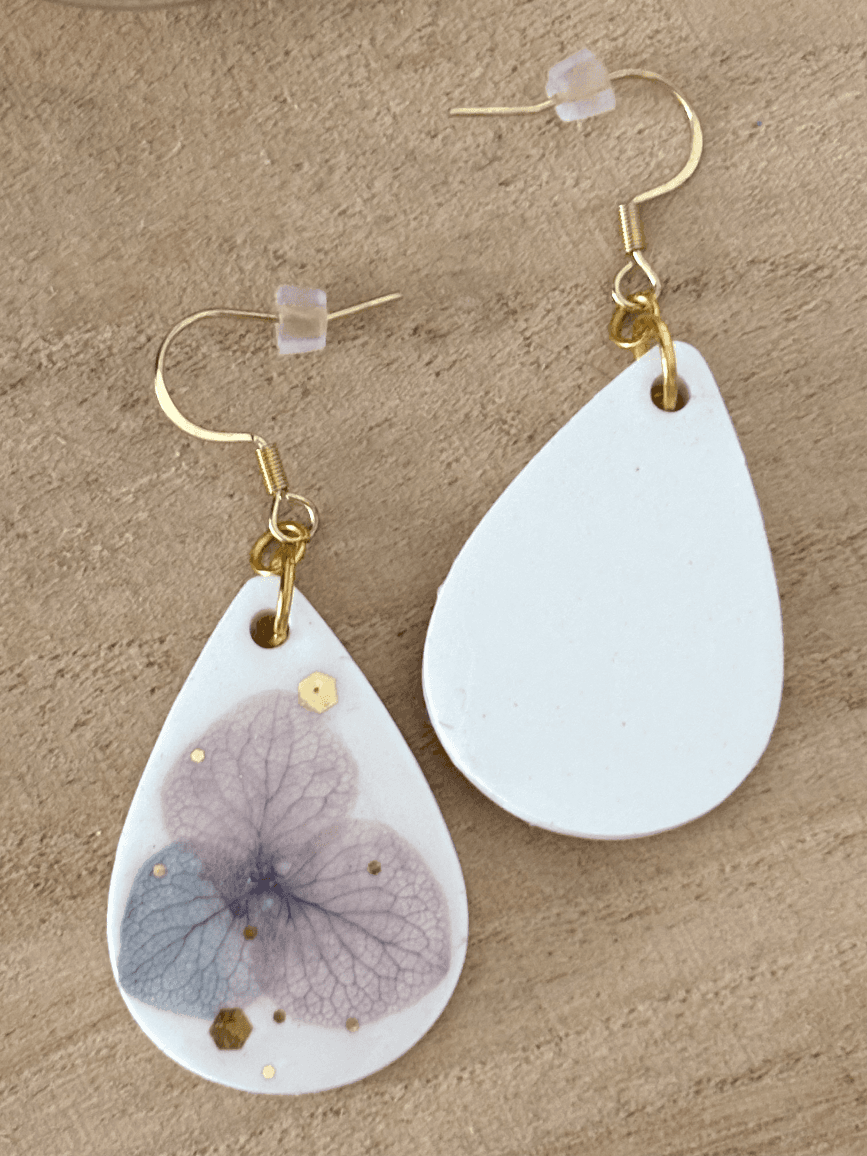 Gros plan sur la résine blanche ornée d'une fleur d'hortensia mauve et de paillettes dorées.