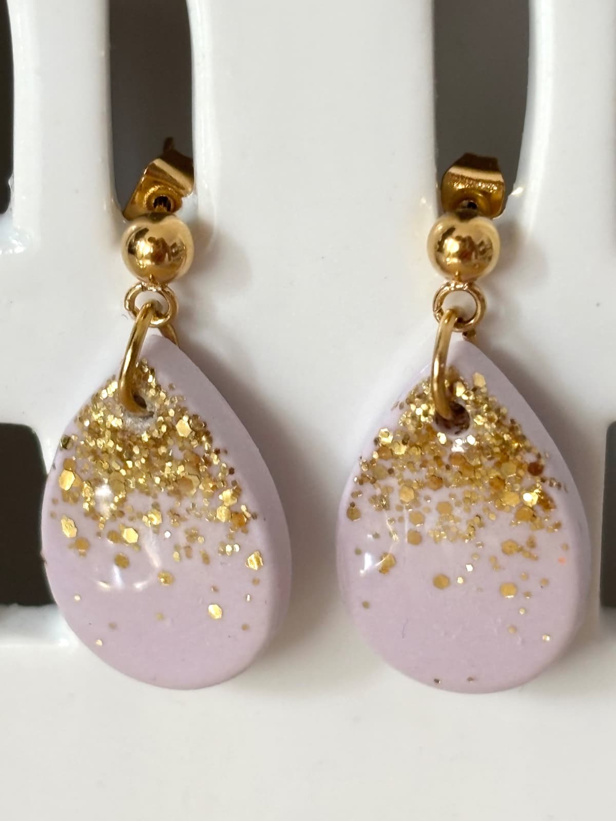 Boucles d'oreilles pendantes gouttes lilas et dégradé de paillettes dorées sur présentoir blanc
