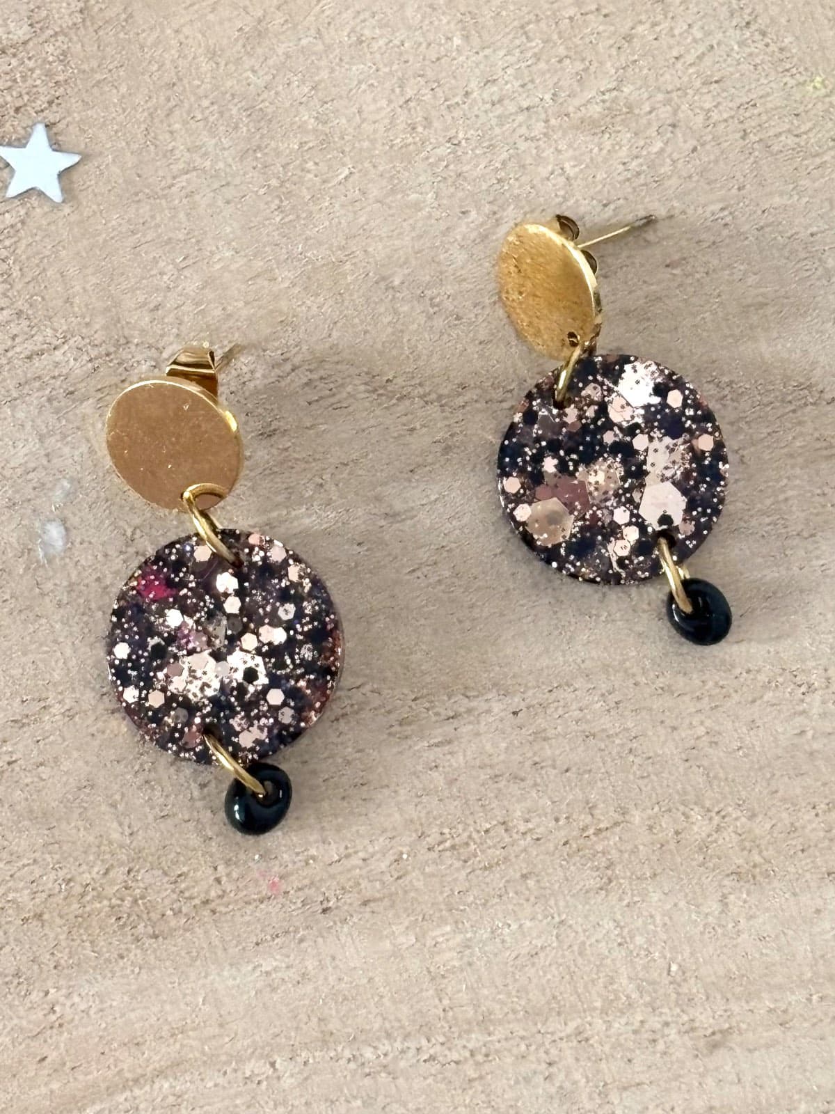Paire de boucles d'oreilles pendantes rondes pailletées noir et or sur fond bois