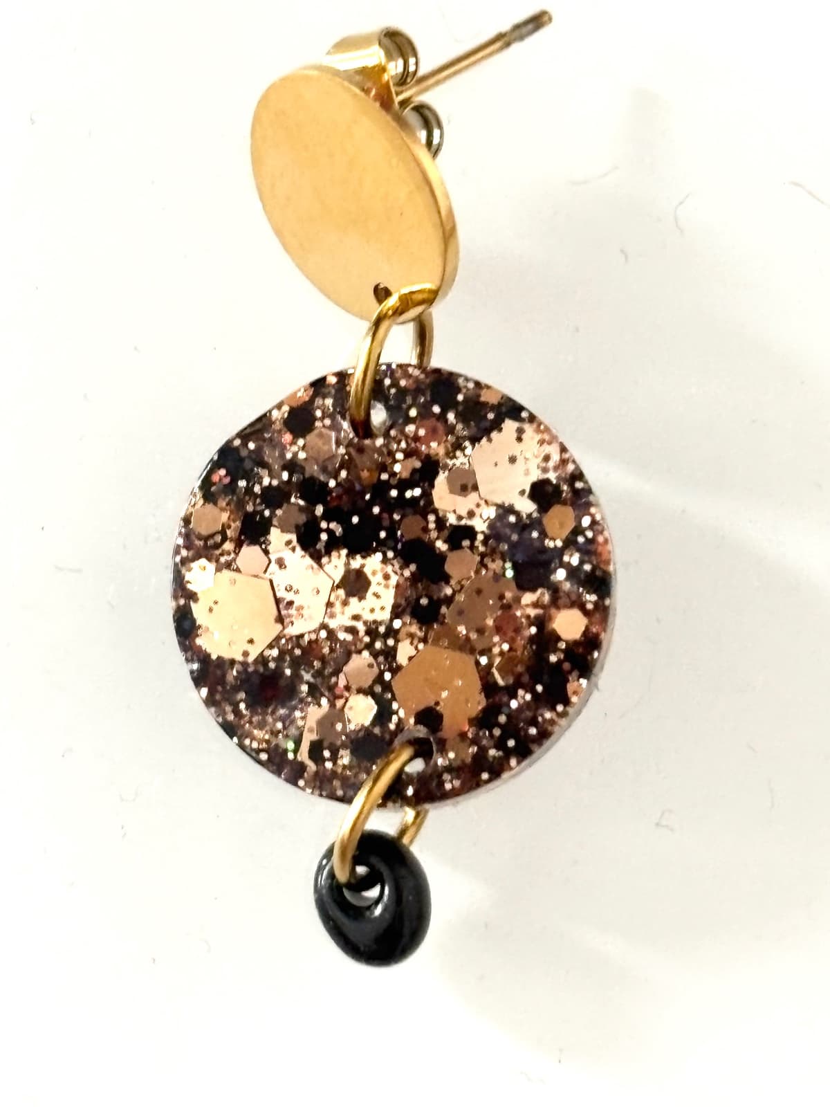 Gros plan sur une boucle d'oreille ronde à paillettes noires et dorées avec perle noire