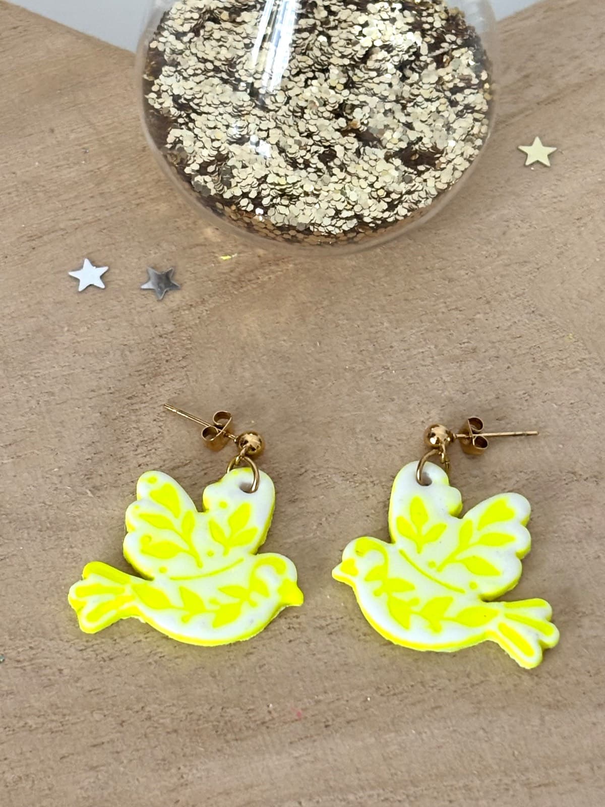 Boucles d'oreilles oiseaux blanches et jaune néon posées à plat sur une surface en bois.