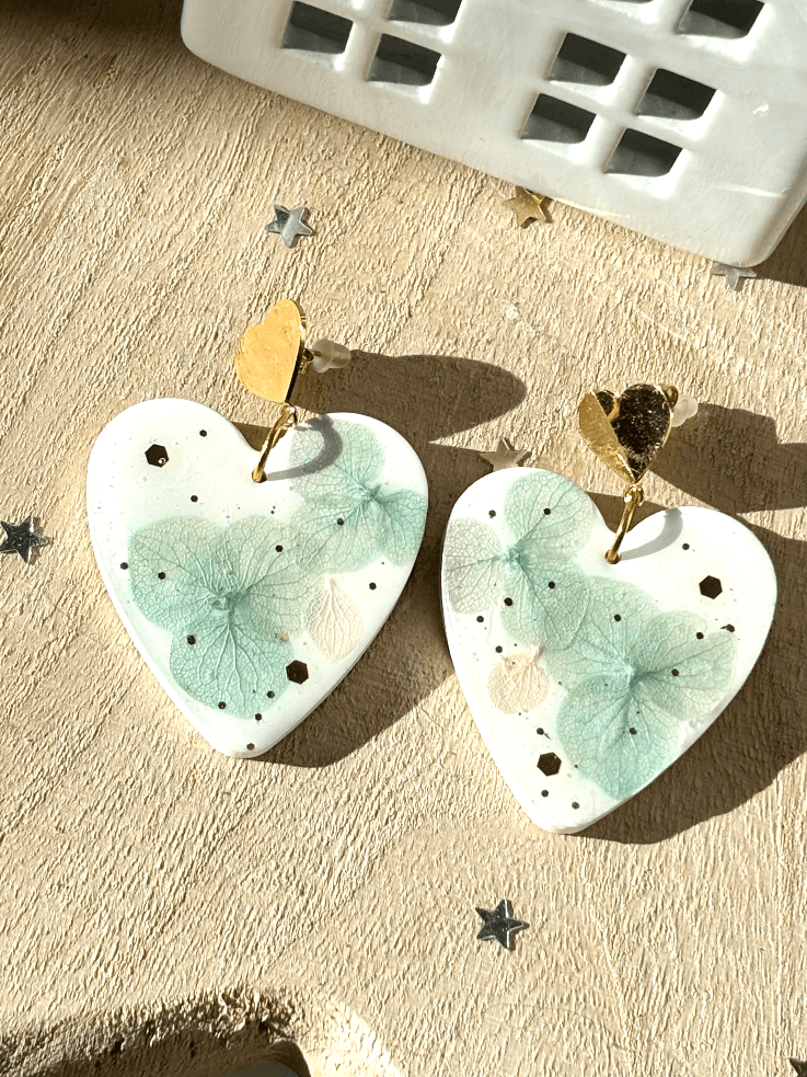 Paire de boucles d'oreilles cœur en résine blanche avec inclusions d'hortensias vert d'eau posées à plat