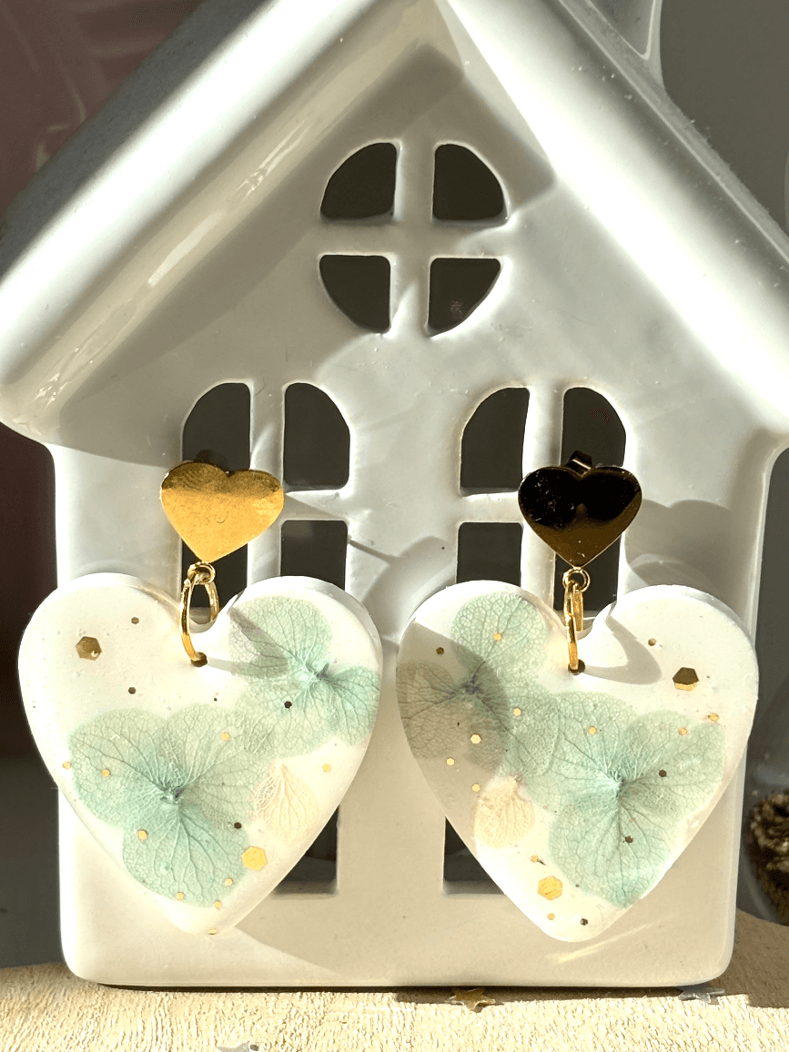 Pendants d'oreilles cœur Bucolique à motifs floraux et attaches dorées suspendus à un support blanc