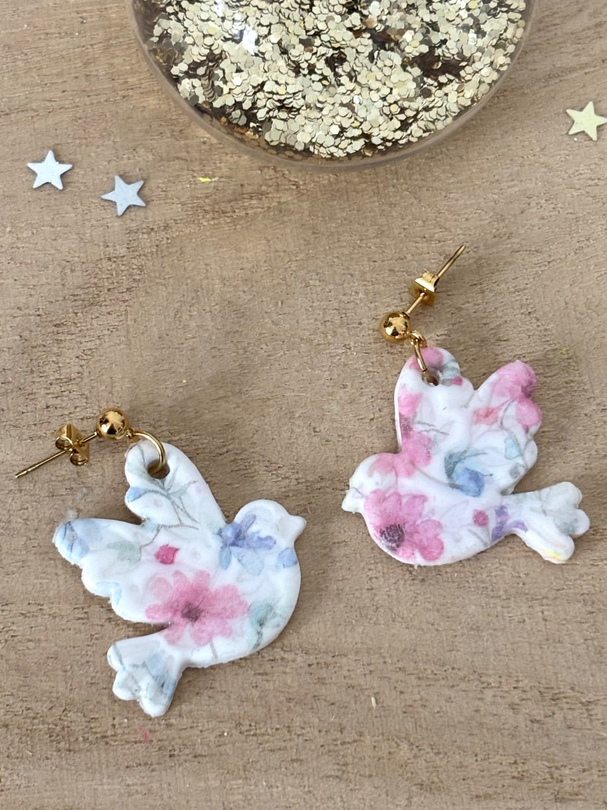 Boucles d'oreilles pendantes en forme d'oiseaux blancs à motifs floraux roses et clous dorés sur fond bois