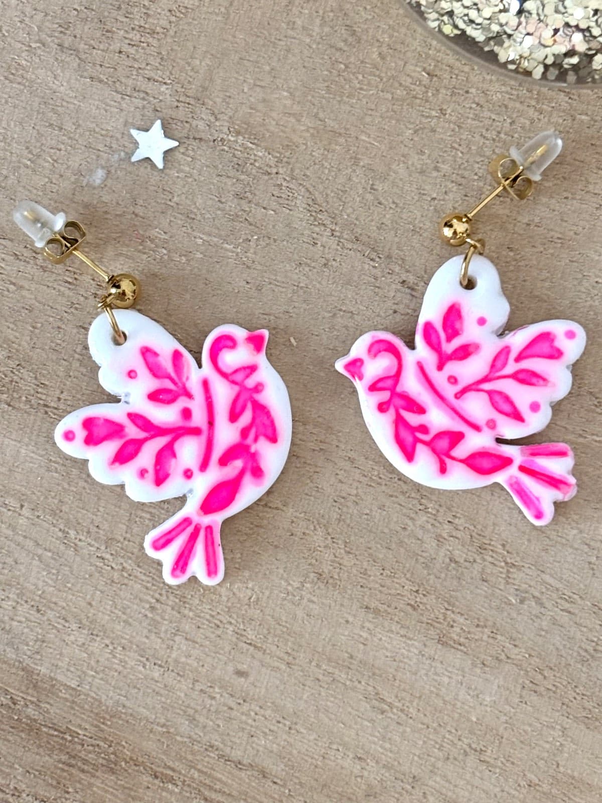 Gros plan sur les boucles d'oreilles pendantes en forme d'oiseaux blancs aux motifs roses vifs.
