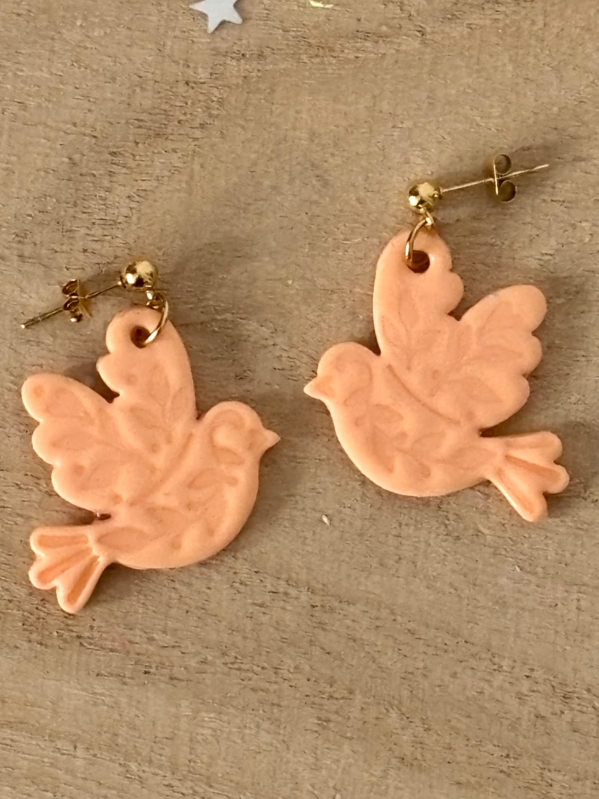 Boucles d'oreilles pendantes en forme d'oiseaux couleur pêche posées sur fond bois