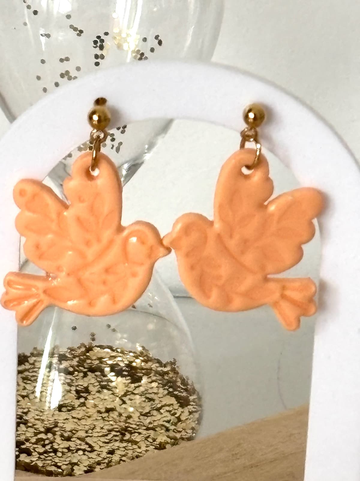 Boucles d'oreilles oiseaux pêche pastel suspendues sur un présentoir blanc