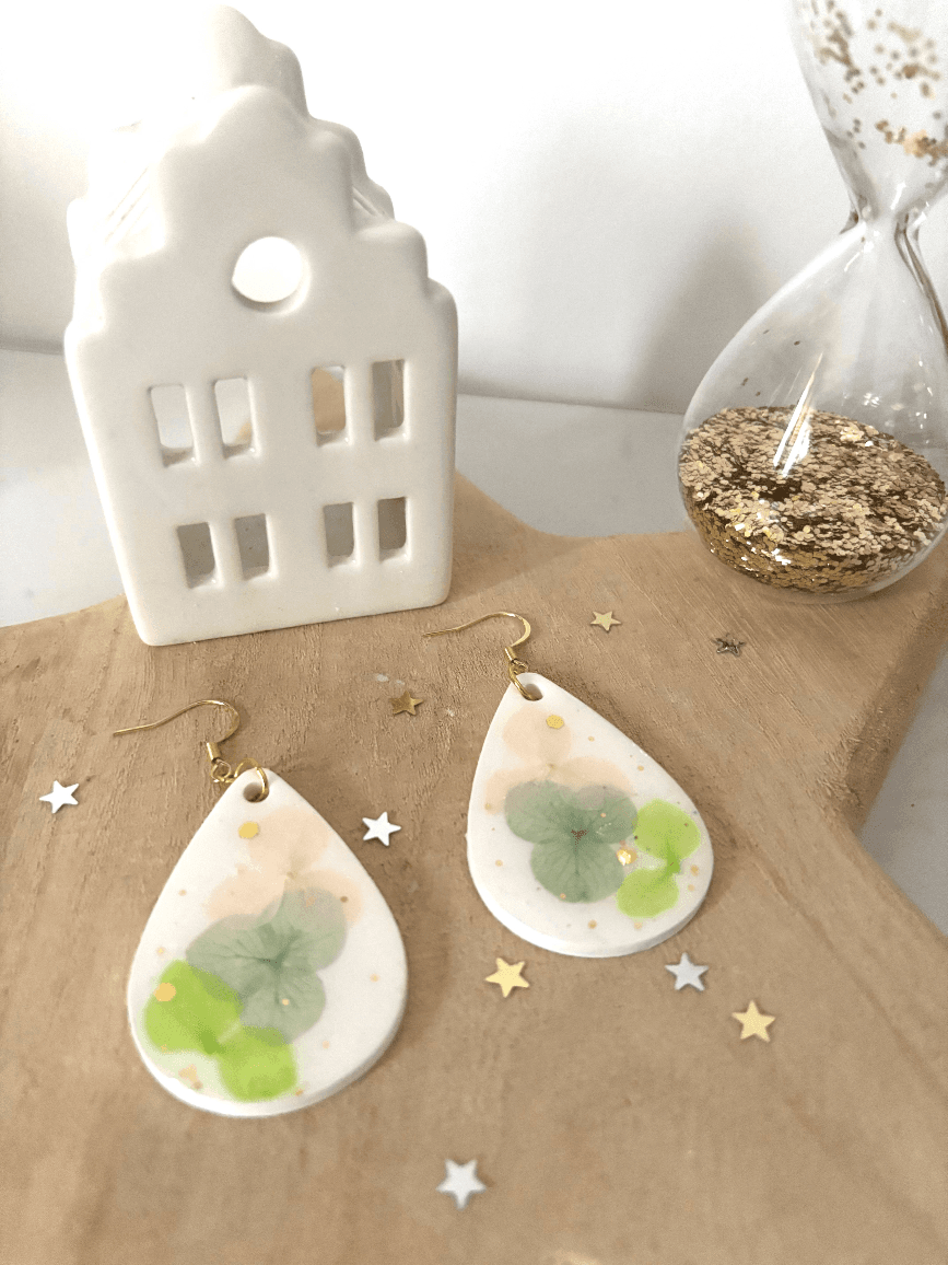Boucles d'oreilles Bucolique posées sur du bois avec un petit décor de maisonnette et sablier doré.