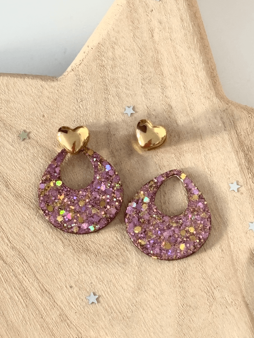 Boucles d'oreilles modulables montrant un cœur doré séparé de sa pampille ajourée rose pailletée.