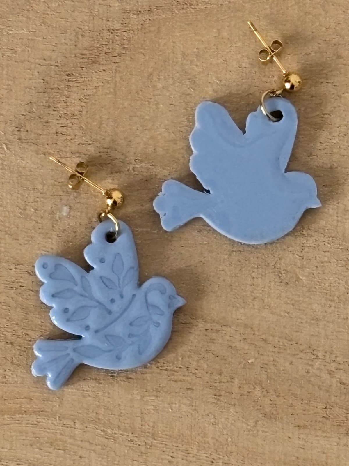 Paire de boucles d’oreilles oiseaux bleu gris sur bois, montrant l’avers à motifs et le revers uni.