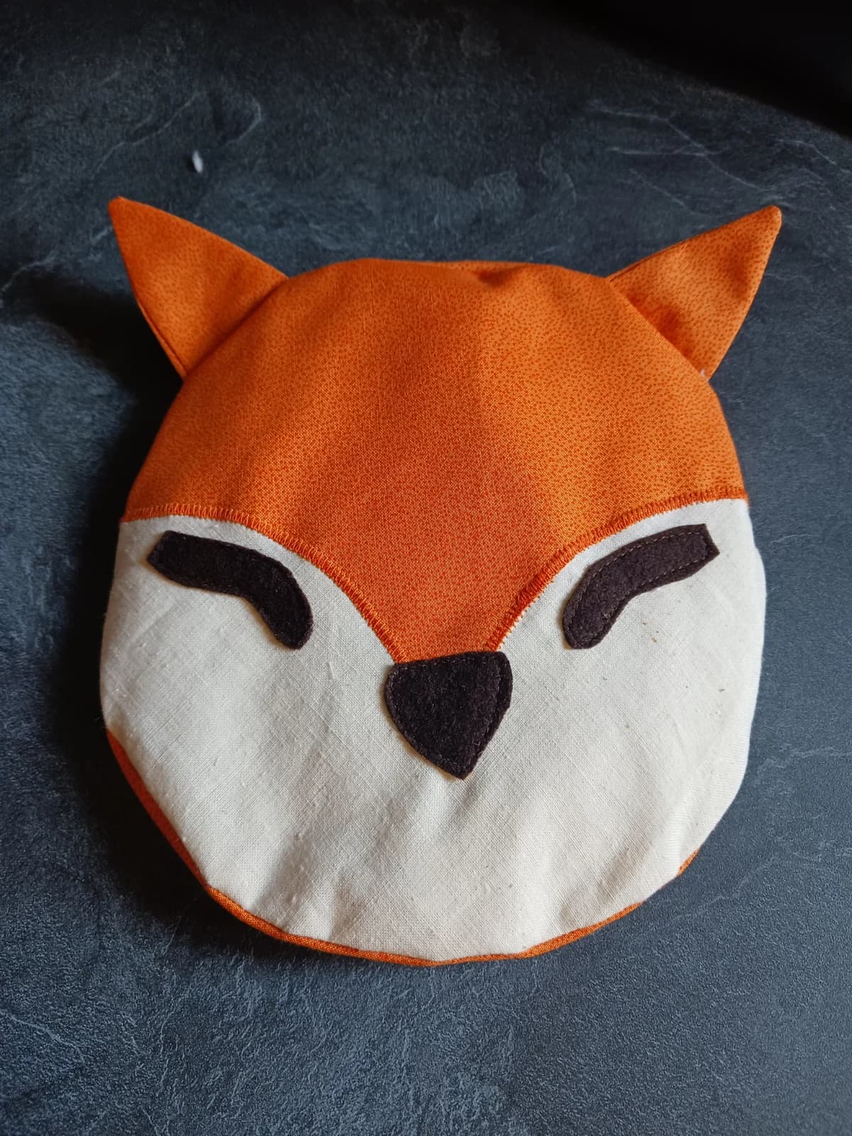 Bouillotte en tissu en forme de tête de renard orange et écru aux yeux fermés