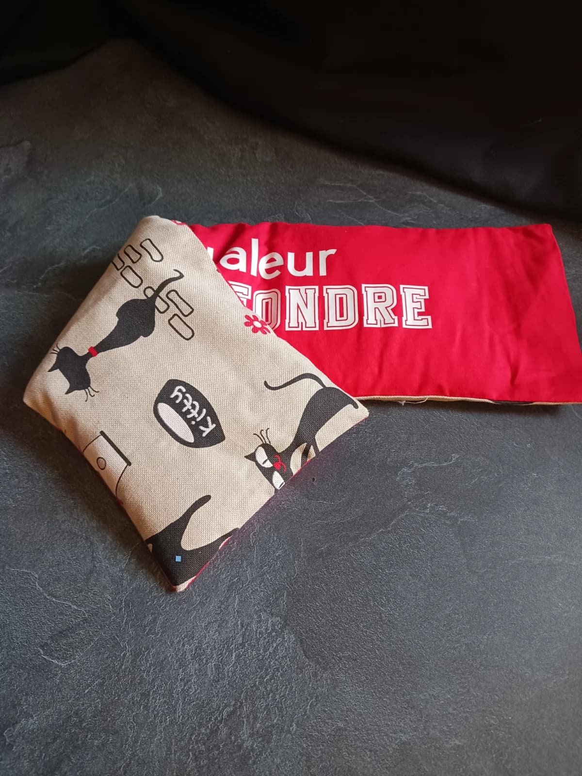 Bouillotte rouge pliée montrant un tissu beige illustré de chats noirs