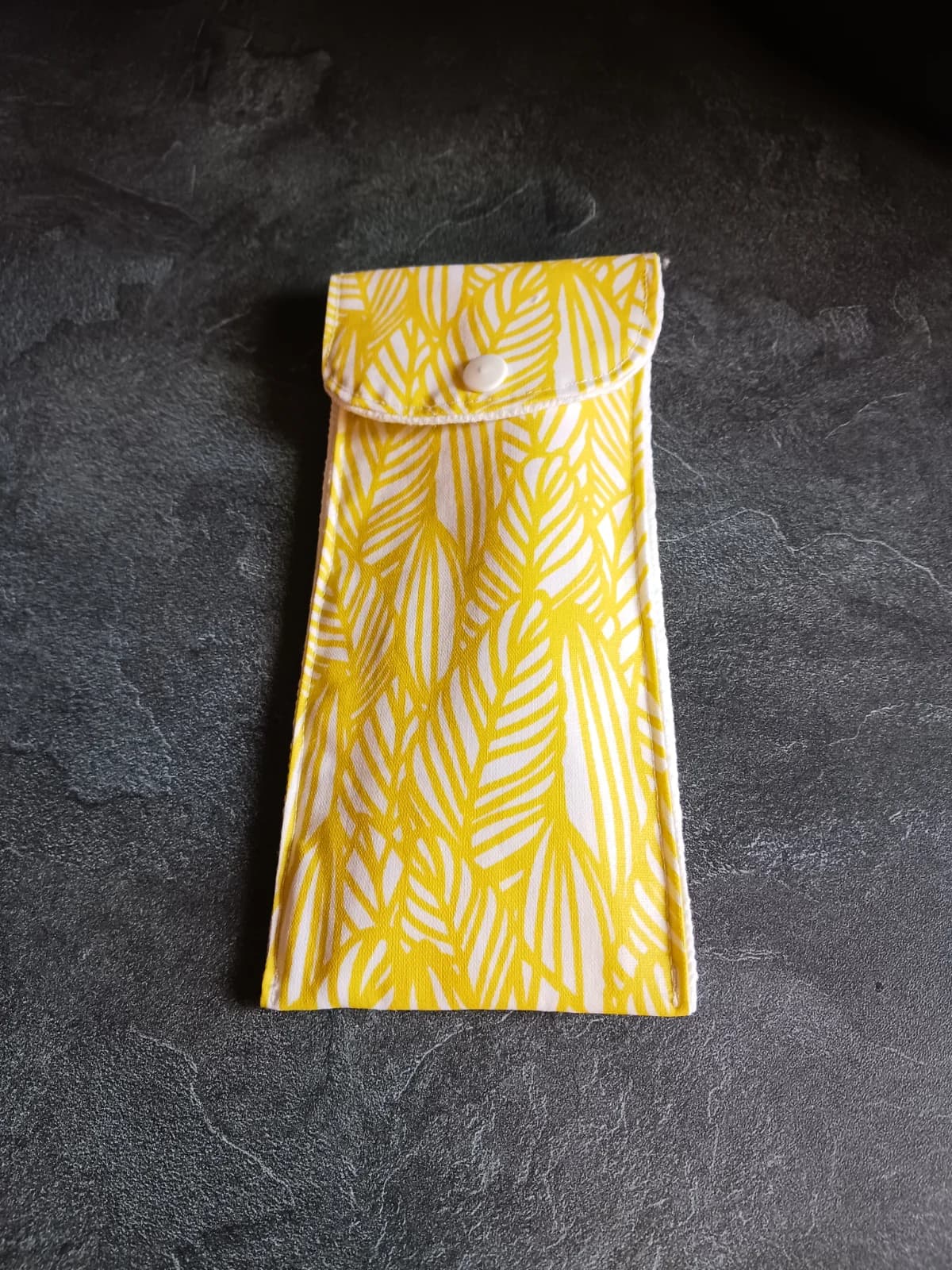 Étui à brosse à dents fermé à bouton-pression avec motifs de feuilles jaunes et blanches.