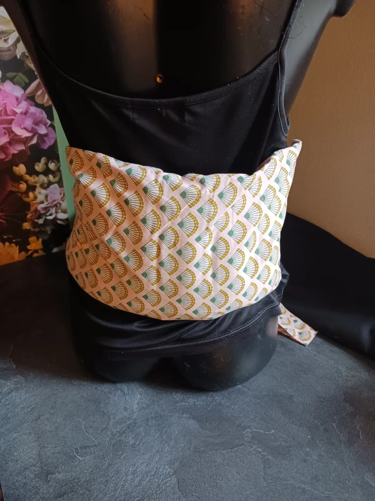 Dos d'un mannequin portant la bouillotte lombaire en tissu rose orné d'un motif éventail vert et doré.