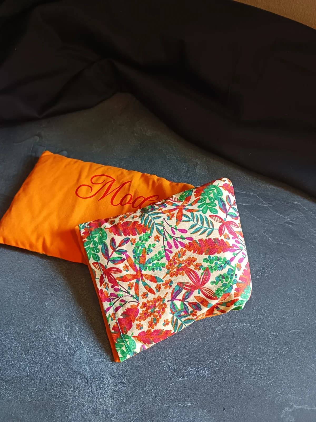 Bouillotte orange pliée avec son coussin intérieur à motifs de feuilles multicolores.