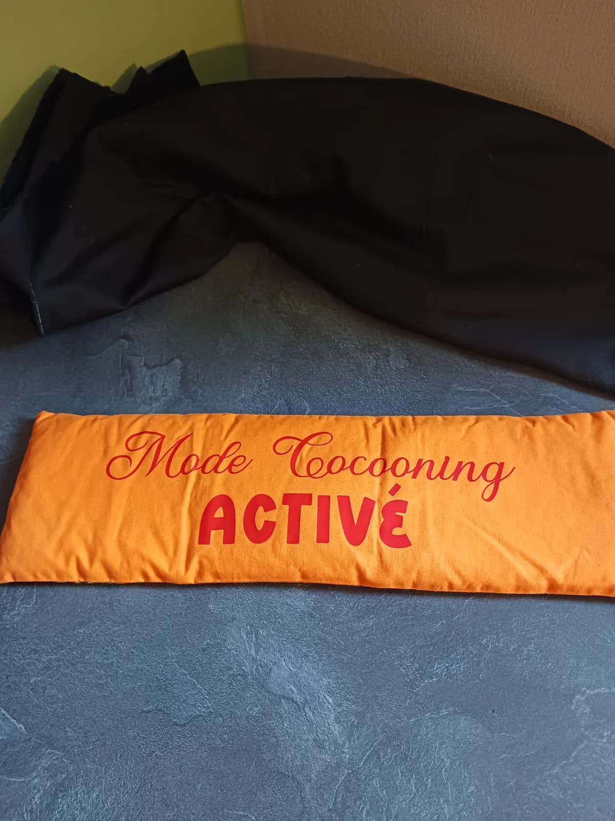 Bouillotte allongée en tissu orange avec inscription rouge Mode Cocooning ACTIVÉ posée à plat.