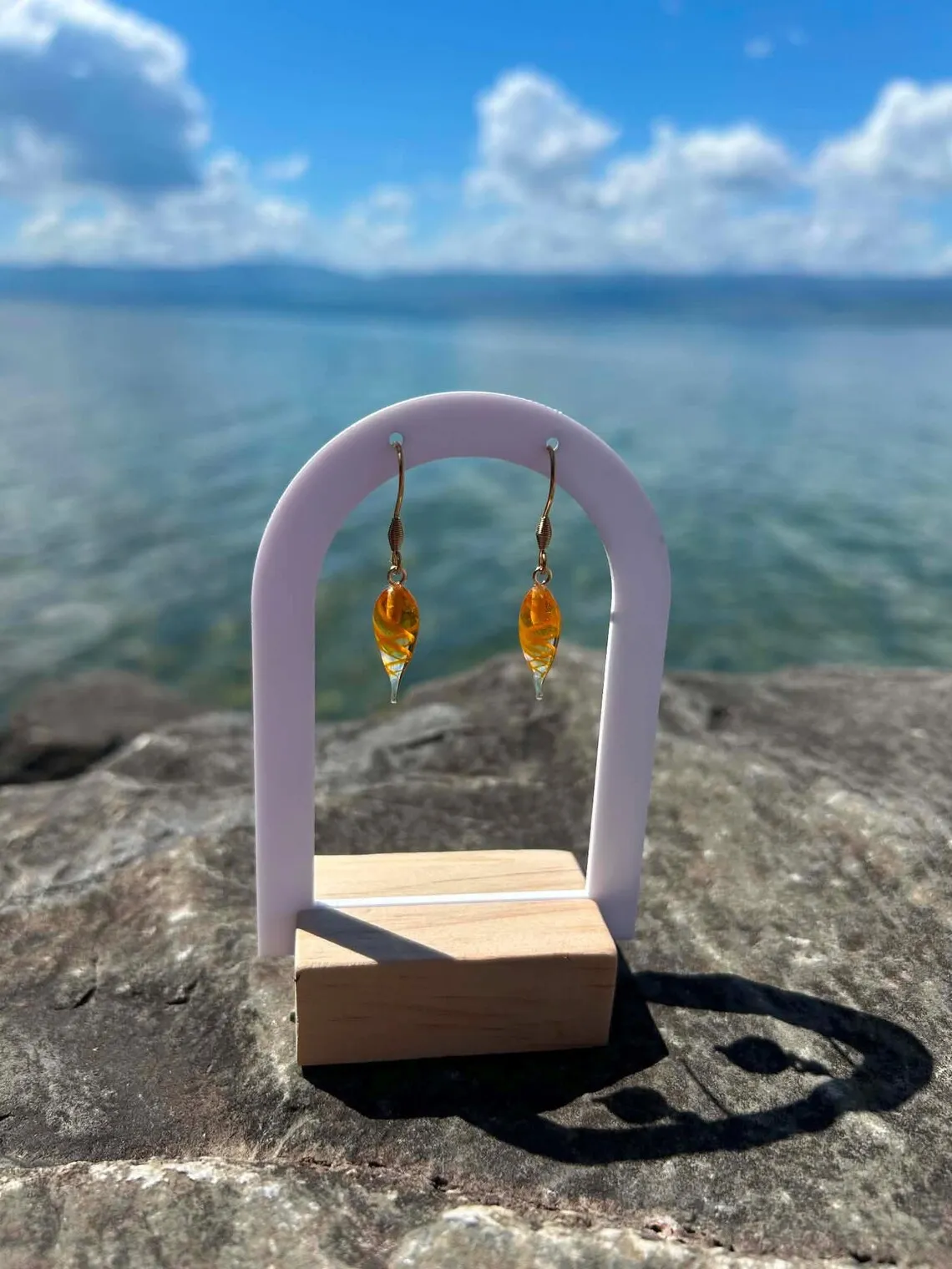 Boucles d'oreilles pendantes en verre filé orange torsadé sur un présentoir en bois et arche blanche.
