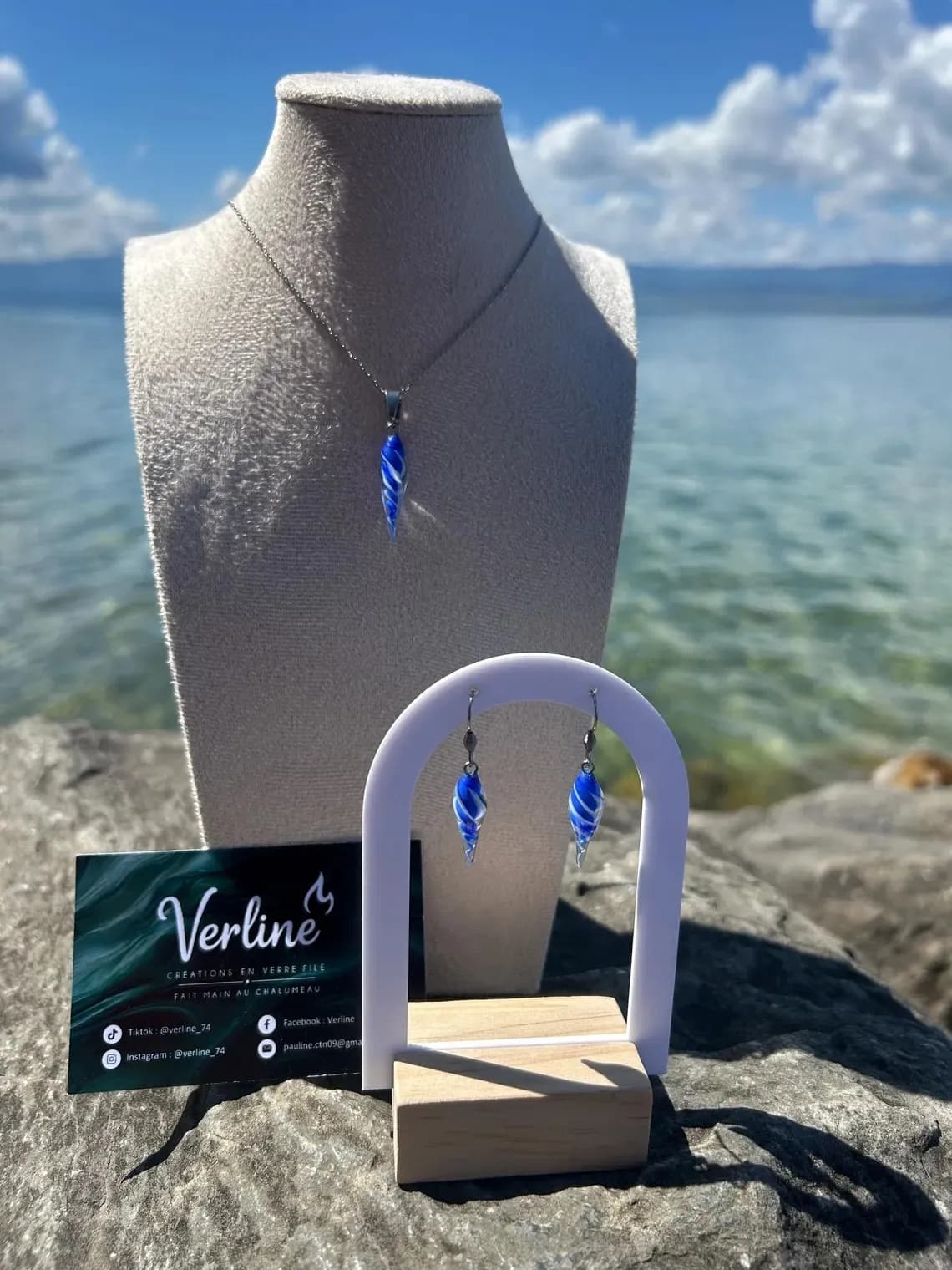 Collier coquillage bleu sur buste et boucles d'oreilles assorties présentées au bord de l'eau.